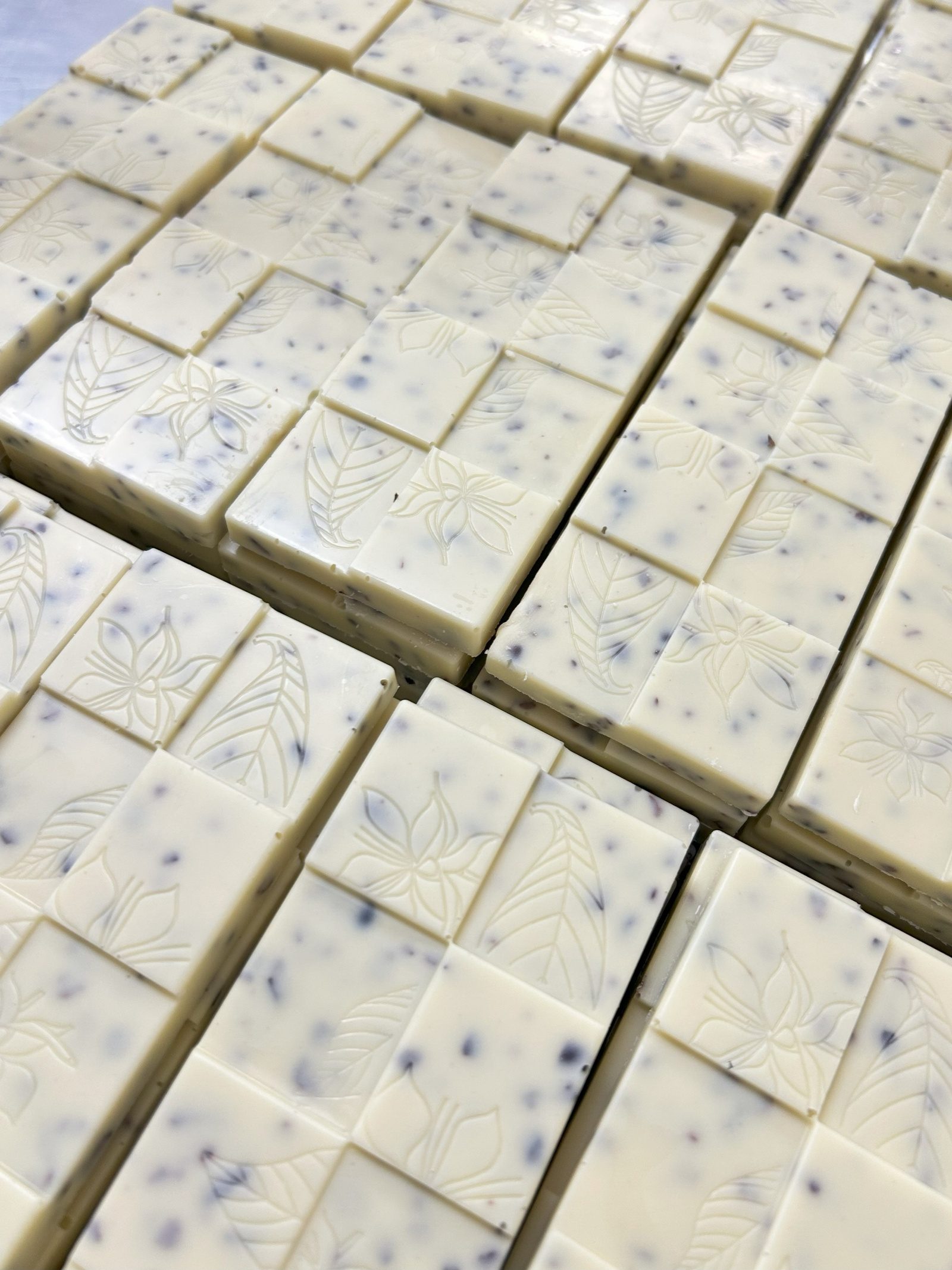 Rows of white chocolate bars speckled with cacao nibs and embossed with leaf and flower patterns