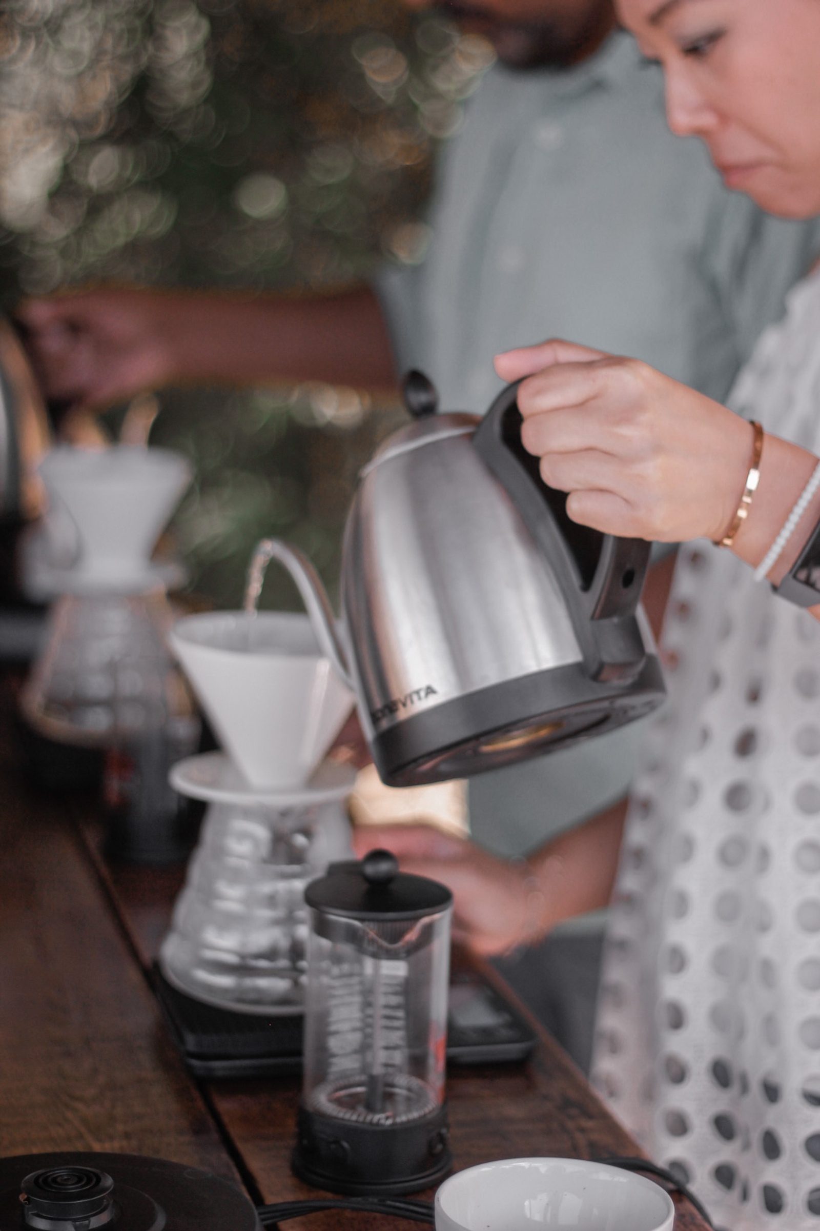 A guest pouring hot water from a gooseneck kettle into a white pour-over cone during the brewing class
