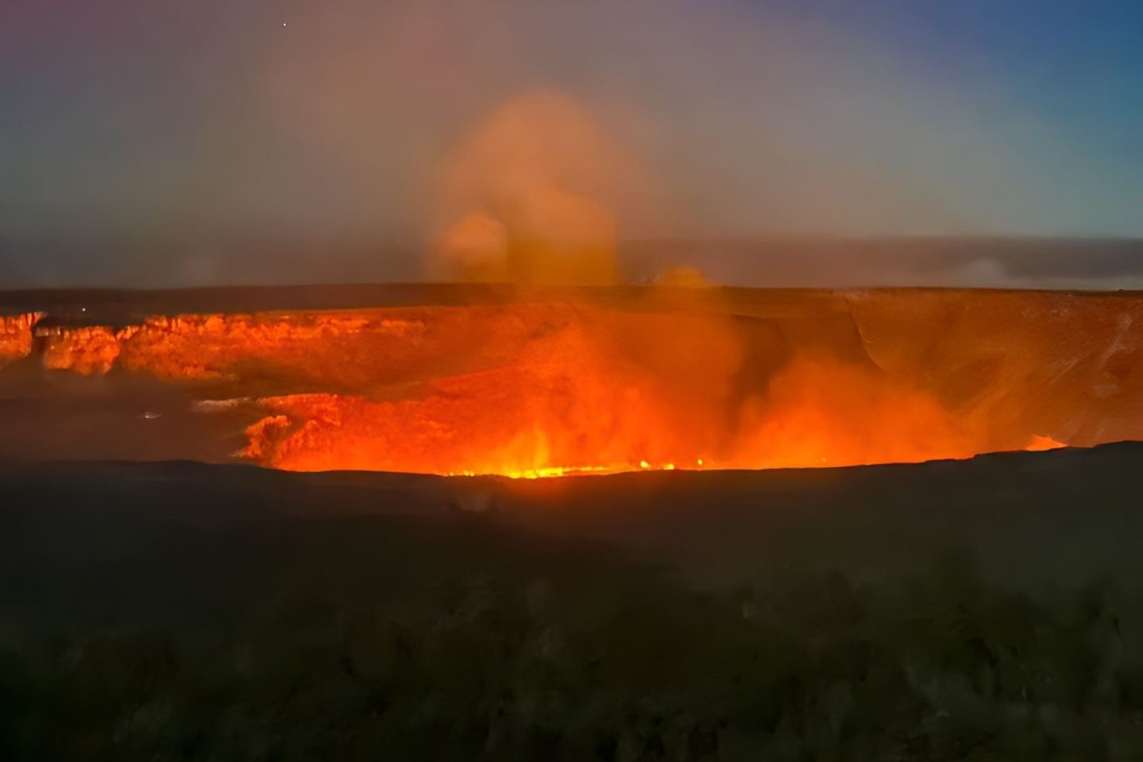A volcanic crater glowing bright orange at dusk under a rising plume of gas and steam
