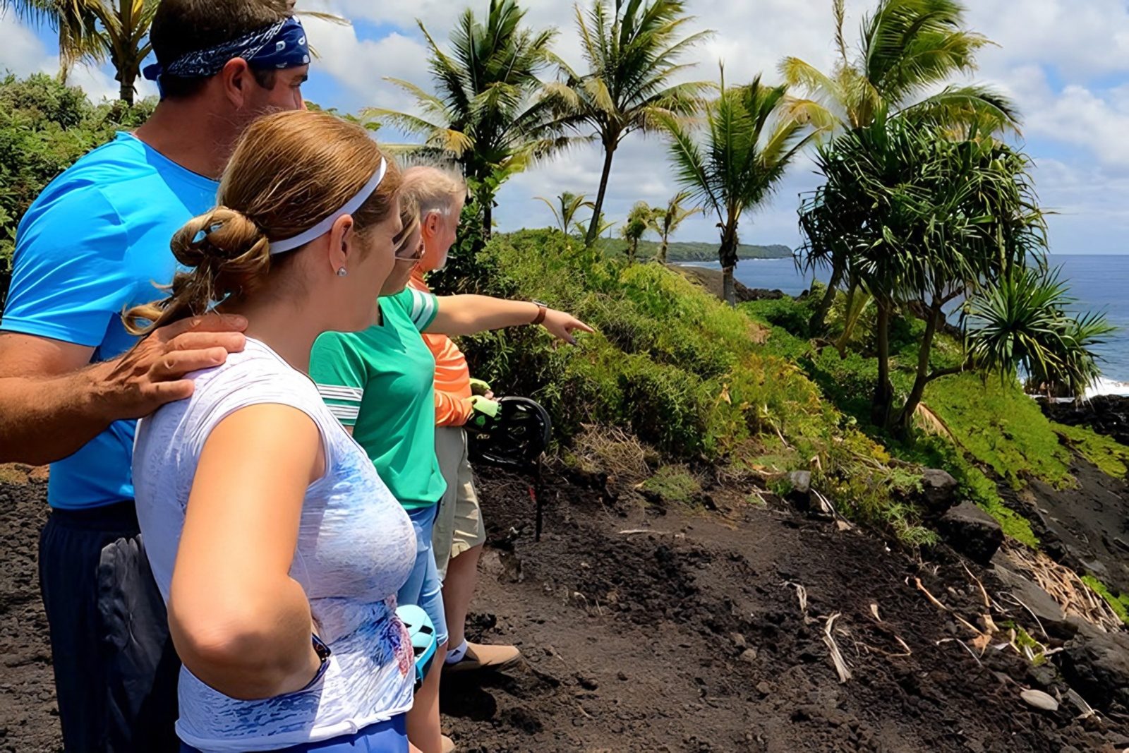 A family of riders on a lava-rock bluff as one points out along a palm-lined coast toward the ocean