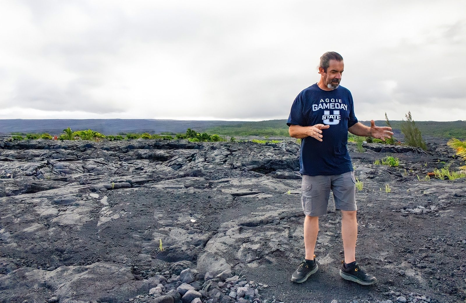 A guide standing on a field of rippled black pāhoehoe lava, using his hands to explain how the flow moved